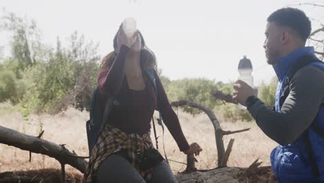 Happy-african-american-couple-sitting-on-tree-trunk-and-drinking-water-in-forest,-slow-motion