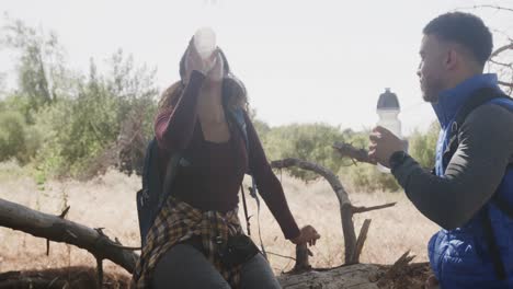 feliz pareja afroamericana sentada en el tronco de un árbol y bebiendo agua en el bosque, cámara lenta