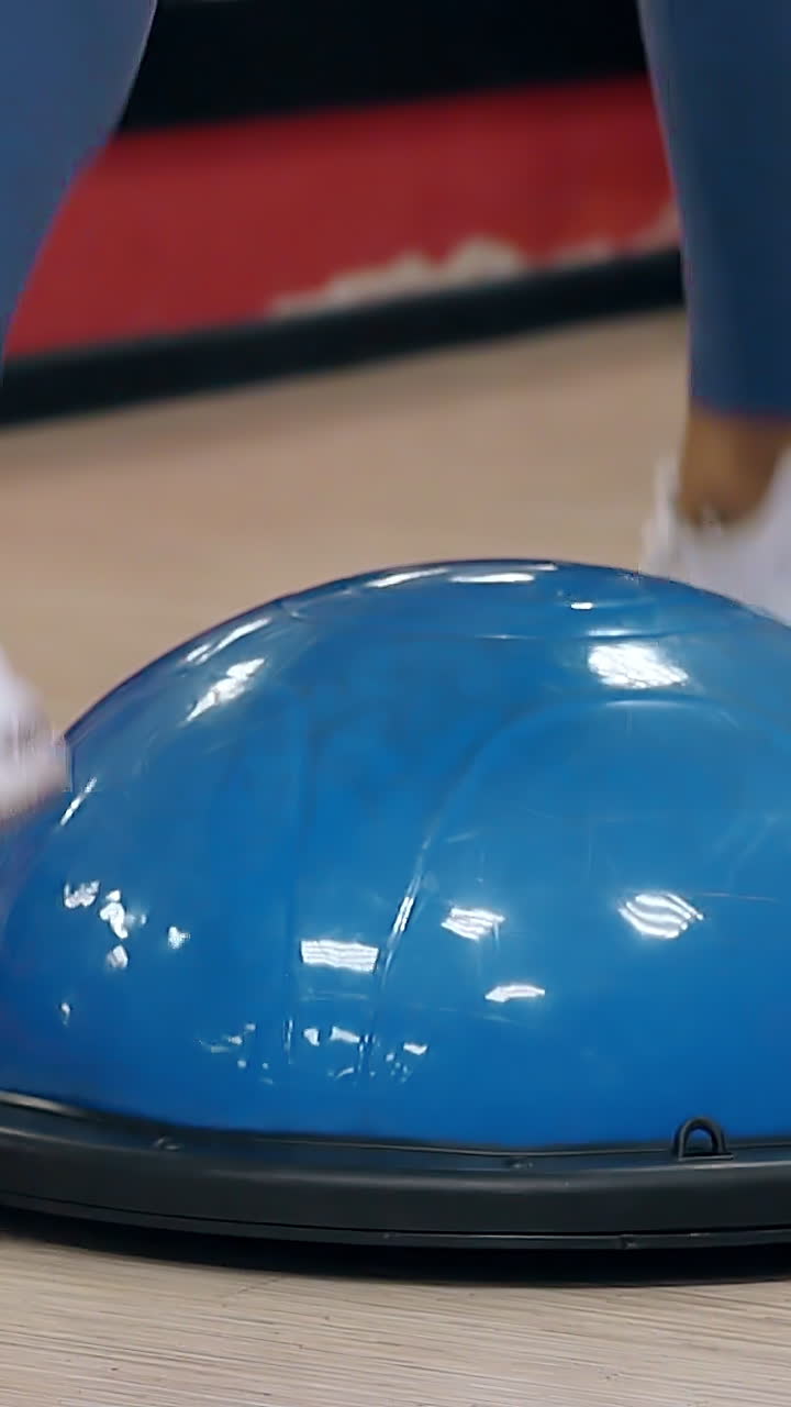 slow motion close view girl slim legs in white sneakers jump on stability ball and ground in gym with red walls