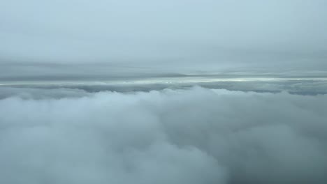 view from a jet cockpit flying between layers of clouds in a cold winter day, near the seashore