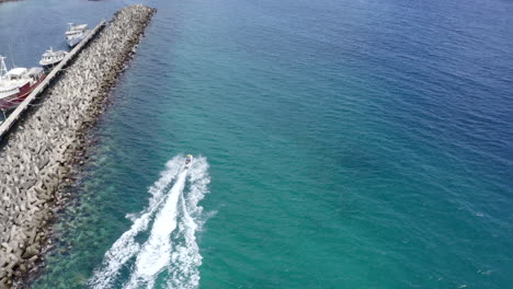 Drone-Barriendo-Un-Jet-ski-En-Barbados,-Bridgetown-Conduciendo-Una-Línea-De-Costa-Más-Allá-Del-Lugar-De-Estacionamiento-De-Botes-Hacia-Las-Playas-De-Bridgetown