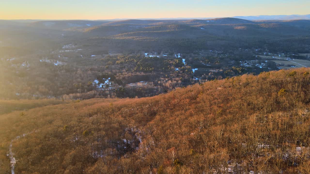 drones volando sobre colinas bañadas por el sol y hacia un valle ligeramente cubierto de nieve, con montañas a lo lejos durante el invierno