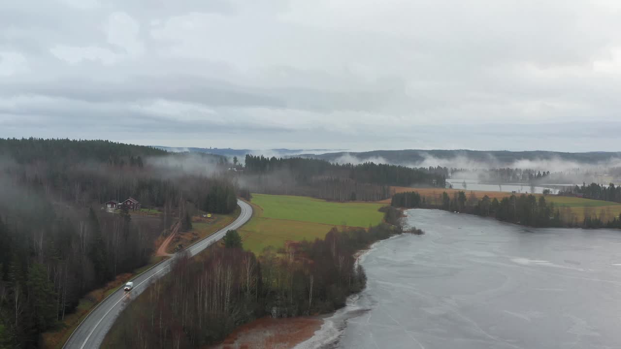 Ruotsalainen maisema, jossa pieni tie kulkee pilvien peittämän järven rannalla. Ilmakuva.