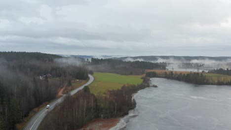 swedish landscape showing a small road next tot a lake covered in clouds. aerial shot