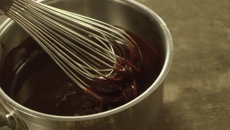 closeup whipping liquid chocolate with metal whisk. macro of chocolate stream.