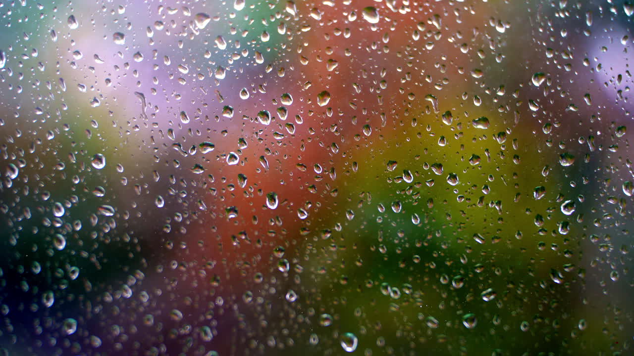 Glass with raindrops. Water drops on window on blurred colorful background. Rain falling outside. Droplets background. Close-up.