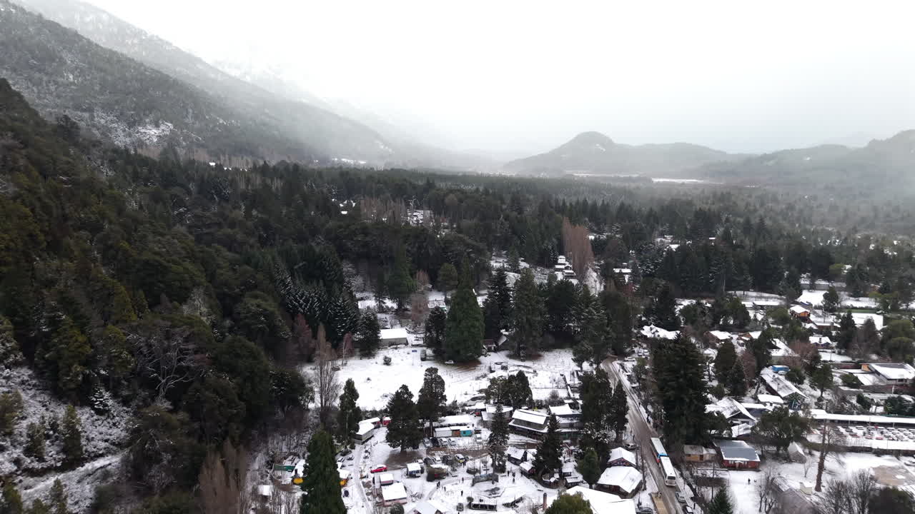 Panorama aerial view of snowy valley of Colonia Suiza settlement surrounded by pine forest and distant mountain ranges, Bariloche, Argentina