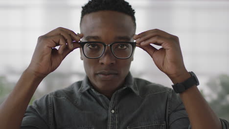 portrait of young male african american business student intern looking serious at camera puts on glasses smiling cheerful