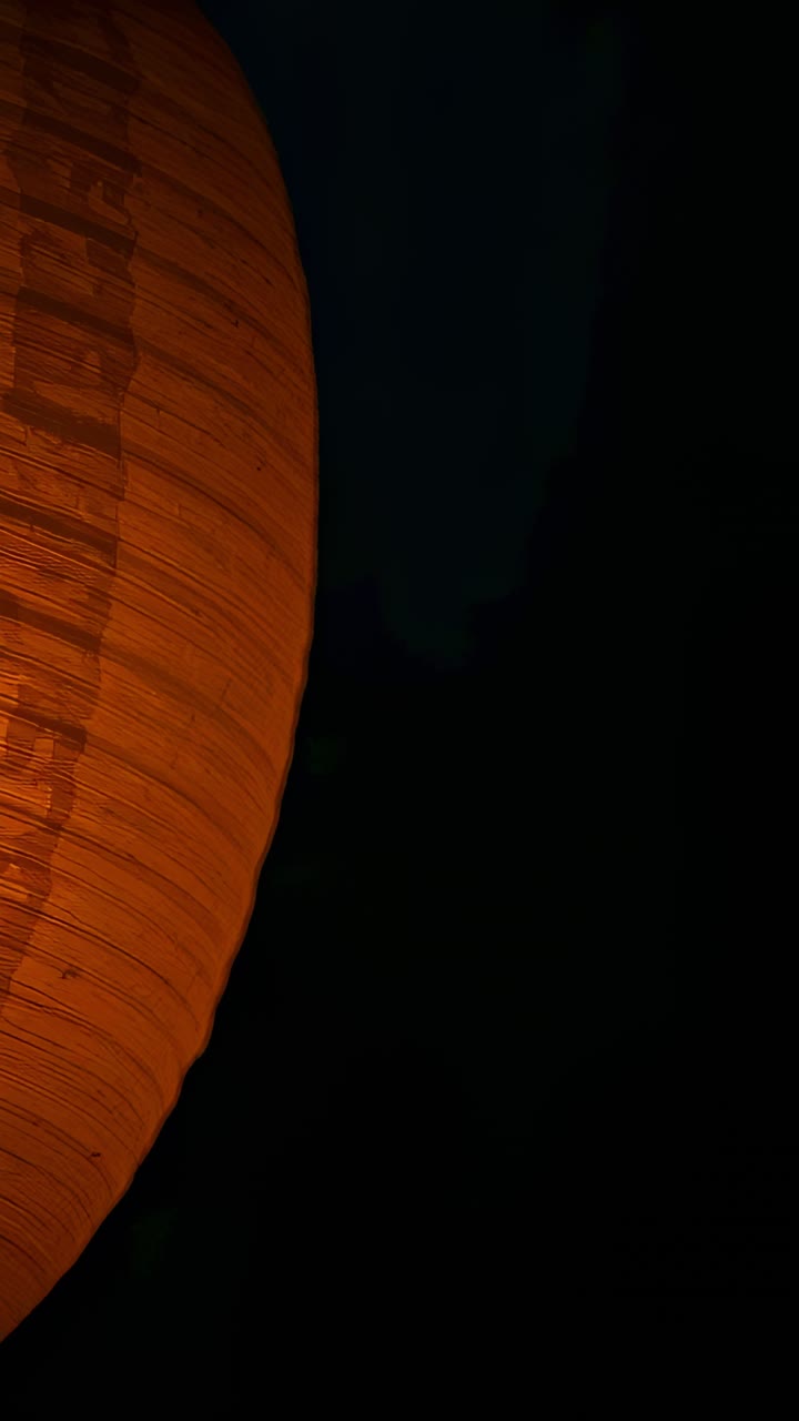 Vertical video: Flickering orange lantern from bulb flicker, casting warm glow at night, copy space