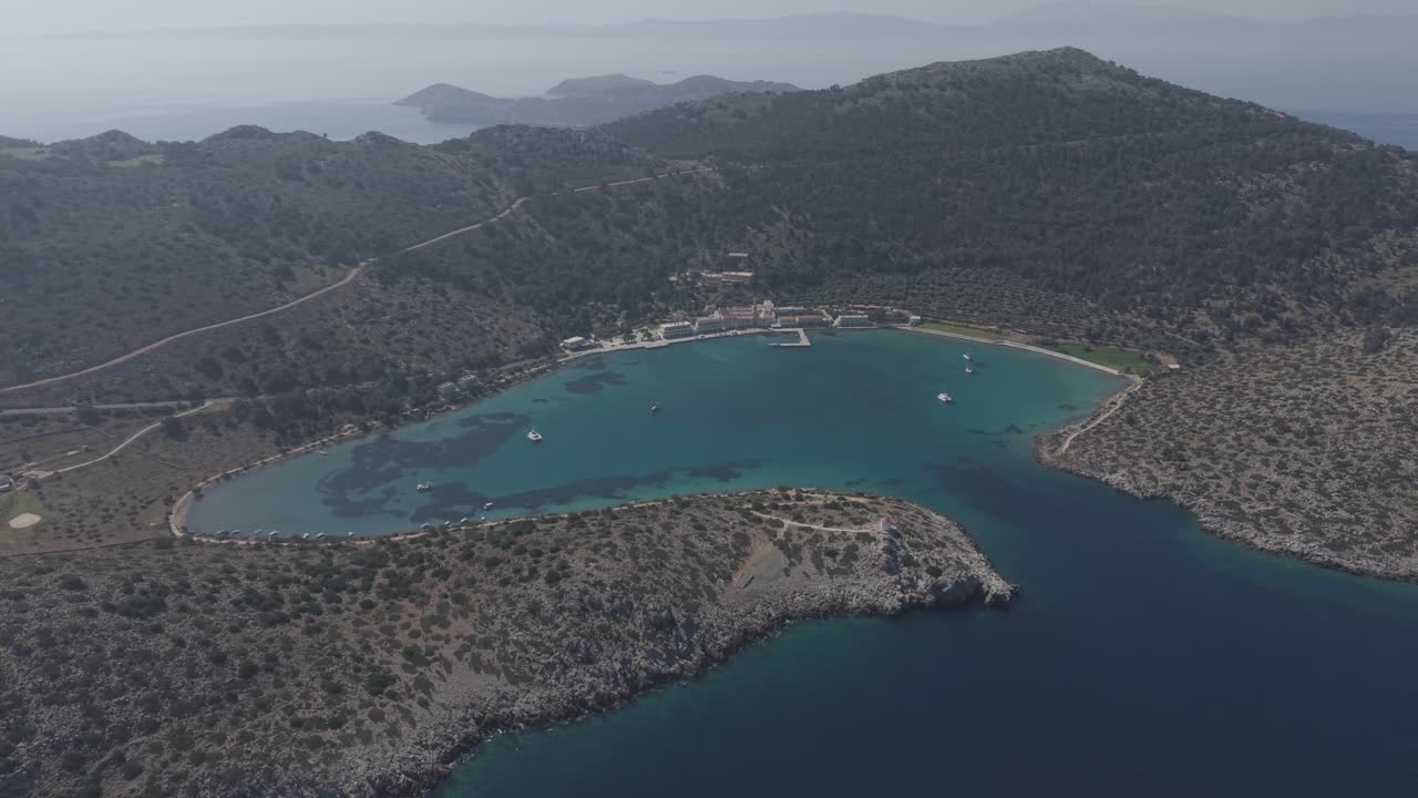 Cinematic drone shots revealing the sacred grounds of Archangel Michael Monastery at Panormitis bay. The aerial view captures the monastery's peaceful setting surrounded by pristine waters.