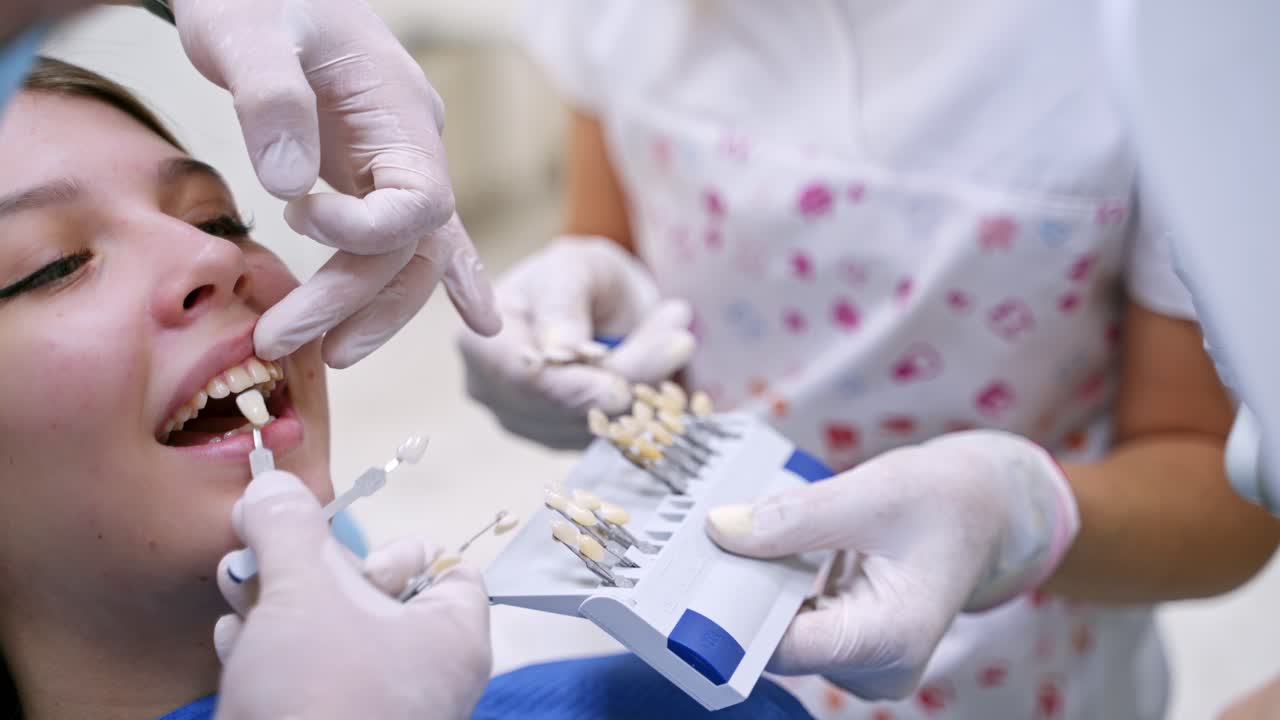 Young female at dentist office. Young lady sitting in dental chair while stomatologist hands in sterile gloves holding tooth samples
