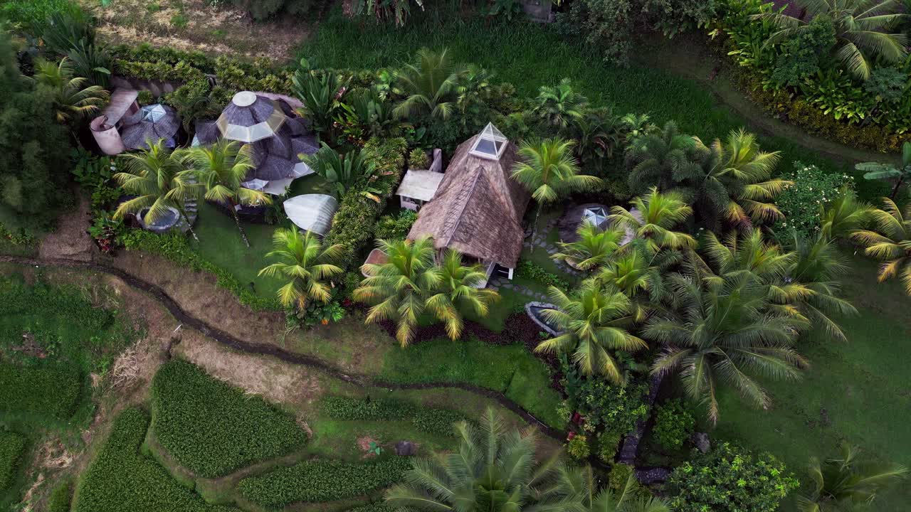 Scenic aerial footage of eco-friendly bamboo retreat nestled among rice terraces, tropical palms, and handcrafted wooden design showcasing sustainable living in Bali’s serene landscape