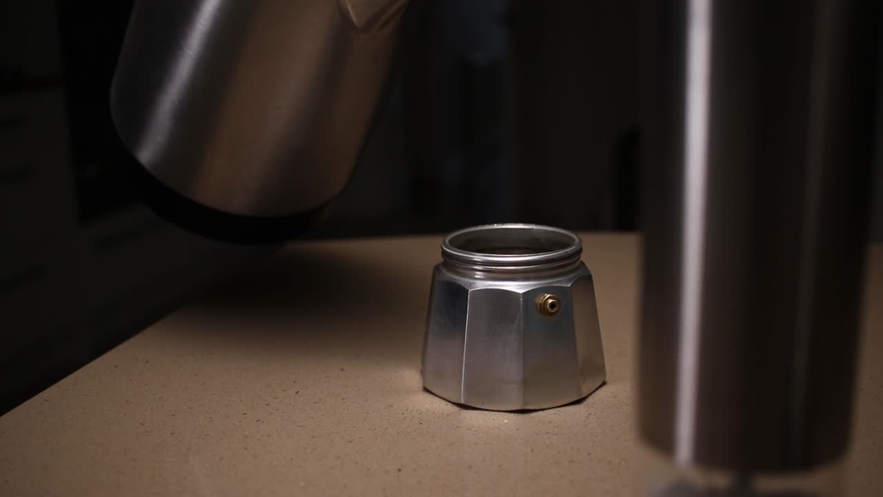 Dolly footage of water being poured into the base section of a Moka stove top Italian espresso coffee maker.
