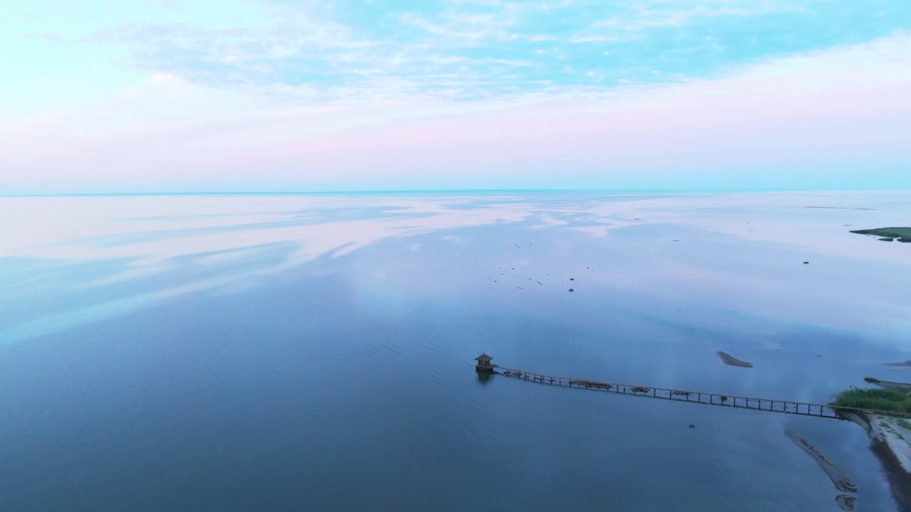 Flying over a calm sea with a pier stretching into the water