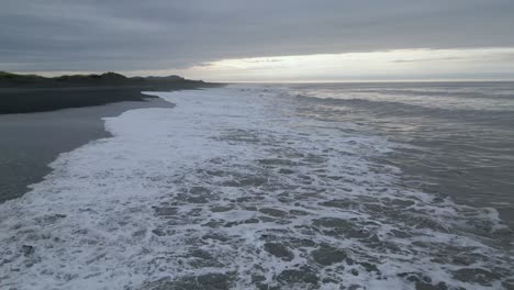 Low-and-fast-flying-drone-flies-over-large-surf-waves-crashing-onto-the-black-sand