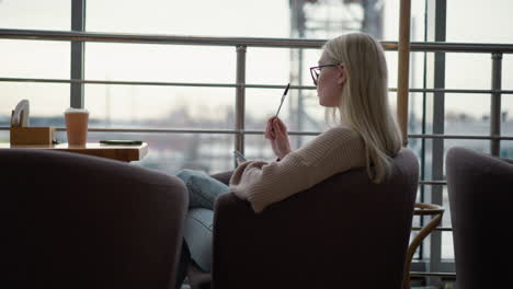 side view of woman seated with a book at a table in a cozy environment, seemingly engaged in reading or writing, with a coffee cup and soft light in the background