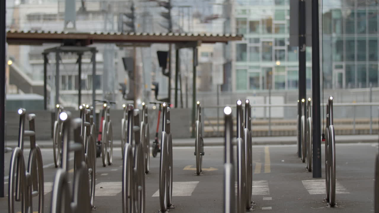 Cinematic medium wide 4K shot with slow parallax motion of illuminated steel bicycle parking stands and the central commerce train station in background, in Barcode Bjørvika Oslo Norway