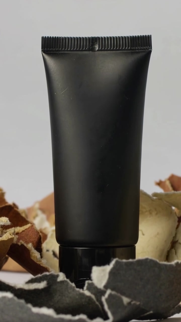 Black Cosmetic Tube with Torn Paper on White Background