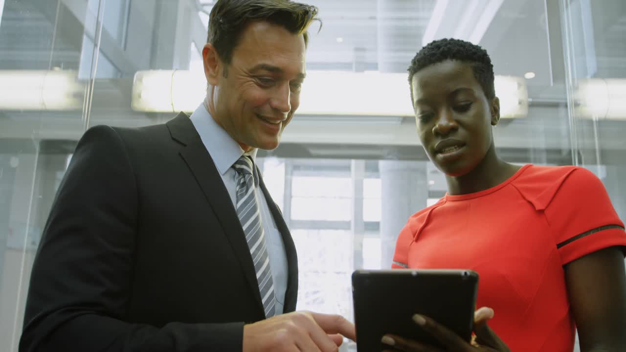 Businessman and businesswoman discussing over digital tablet in elevator 4k