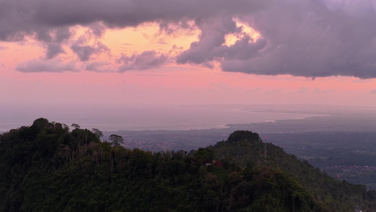La valle di Sidemen si affaccia su un oceano avvolto dalla nebbia sotto nuvole drammatiche e un cielo arancione, con creste montuose boscose in primo piano