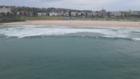 Playa-De-Bondi-Con-Surfistas-Montando-Las-Olas-Con-Los-Suburbios-Del-Este-De-Fondo-En-Sydney,-Nueva-Gales-Del-Sur,-Australia