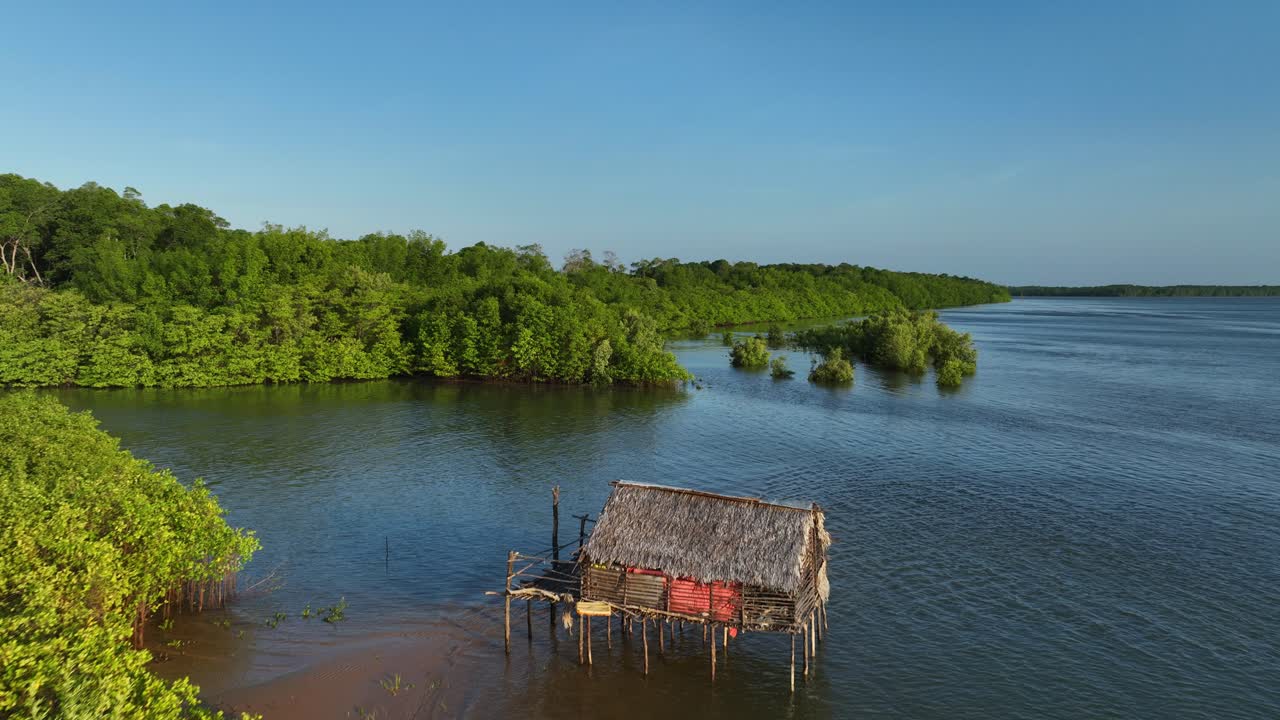 Thatched wooden house in shallow water along the Parnaíba River, surrounded by mangroves in Araioses, Maranhão. Dolly in flyover aerial