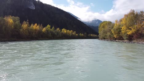 flying along river over water surface with trees growing around, mountains in the distance on a sunny day