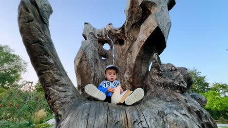 lovely little boy sits on a big wooden sculpture of a cat. kid holds a book but looks around.