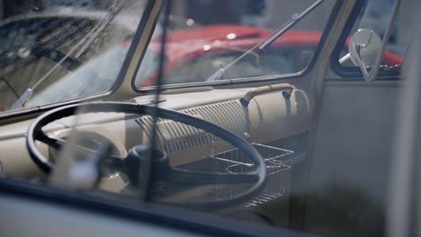 View-into-the-cab-of-a-silver-vintage-car-through-a-window,-on-the-dashboard-and-steering-wheel-on-a-sunny-day