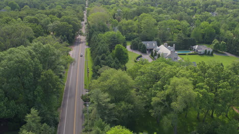 cars travel up and down a road and past a nice house in ladue, aerial view