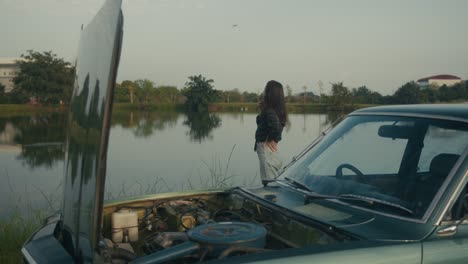 woman by a broken down vintage car by a lake
