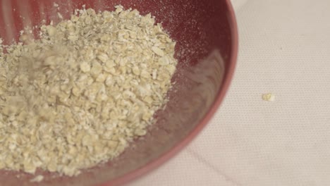 Helping-of-dry-rolled-oats-pouring-into-a-red-bowl