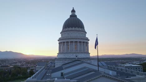 blue flag of the state of utah flutters slowly over the capitol building just after sunset