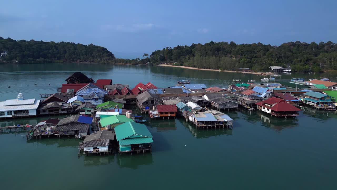 Bang Bao Pier floating village in Koh Chang island, Thailand, showing colorful houses and boats sailing in turquoise water. Nice aerial view flight fly reverse drone