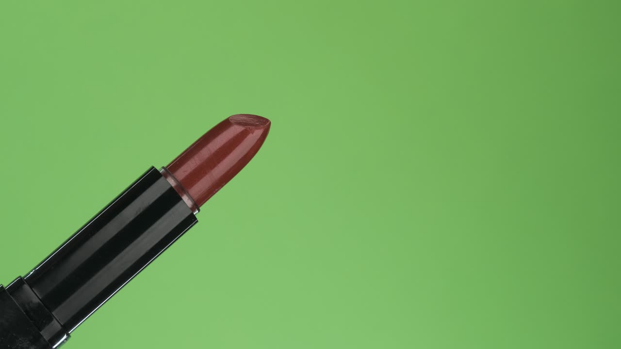 Rotazione diagonale del tubetto di rossetto aperto. Isolato su verde