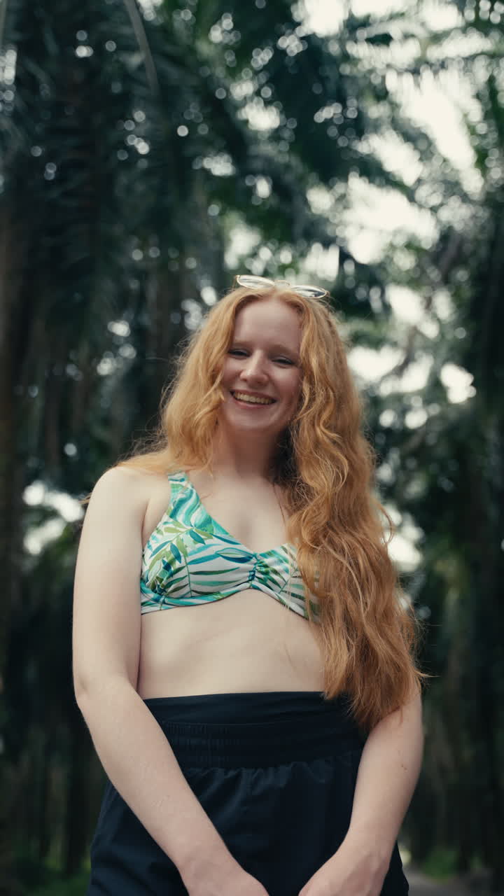Donna dai capelli rossi in top bikini e shorts sorridente all'aperto