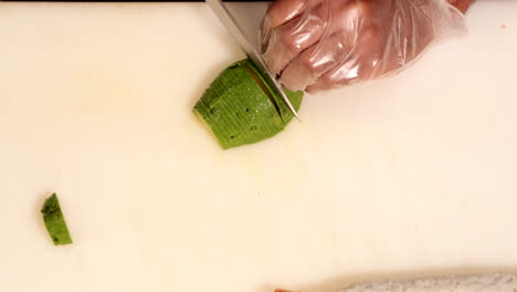 chef cutting fresh green avocado fruit into thin slices for sushi roll making - overhead panning shot