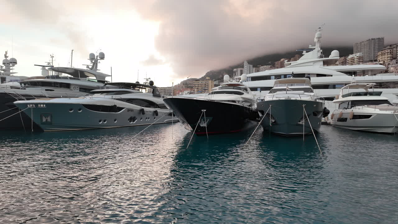 La Condamine, Monaco - July 4, 2025: Row of sleek luxury yachts, docked in Port Hercules with the Monaco cityscape and misty hills in the background
