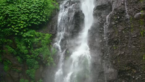 aerial of powerful water falling off rocks covered in moss in the jungle in bali indonesia