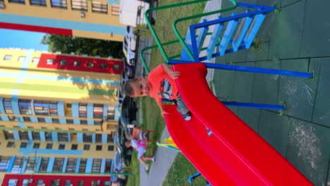 adorable smiling baby boy climb on the slide. cute caucasian kid slides down on the playground. vertical screen.