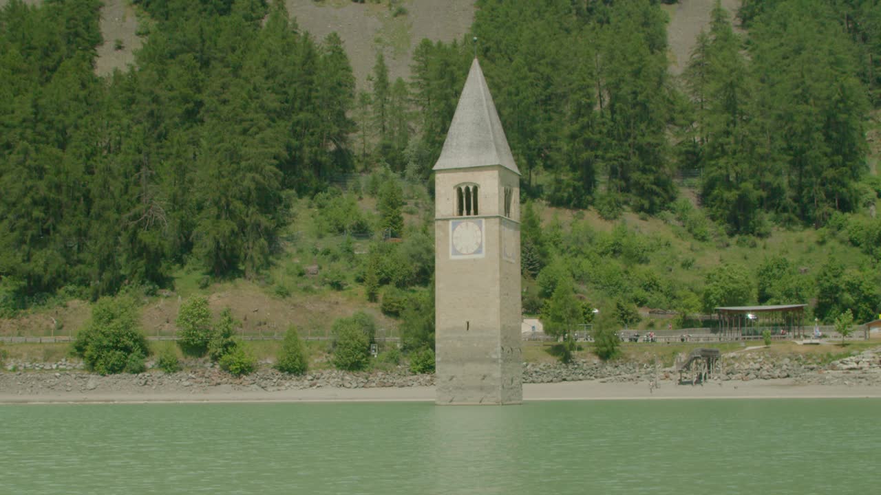 toma completa, vista panorámica de kirchturm von altgraun en italia, costa de reschensee y cordillera forestal en el fondo