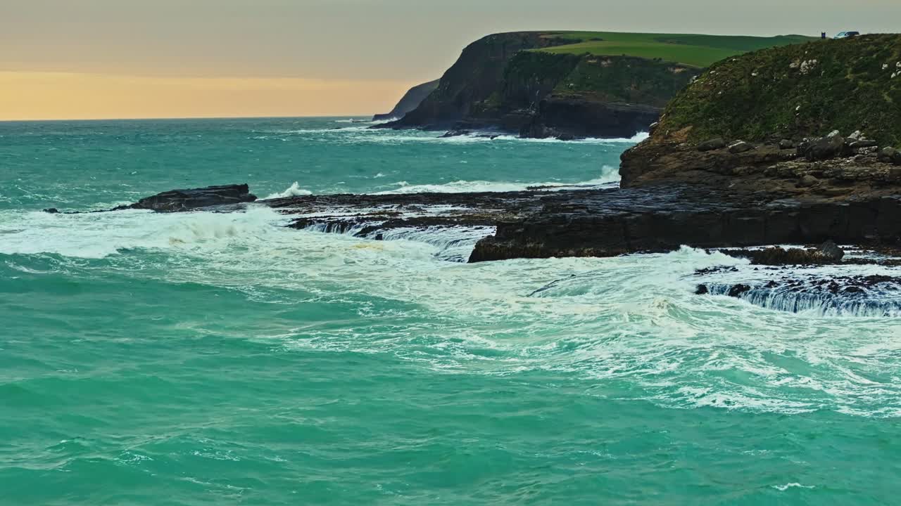 Aerial dolly above rocky shorelines as waves crash and spread water across intertidal zone