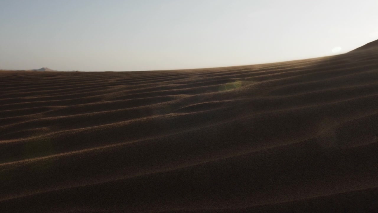 Hiekkaa puhaltaa aavikon hiekkadyynien yli auringonvalon paistaessa Lähi-idän aavikkomaisemassa lähellä Dubaita Yhdistyneissä arabiemiirikunnissa