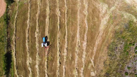 Aerial-view-of-an-blue-tractor-lining-down-animal-provisions-ready-for-collection,-steady-camera,-4K,-60fps