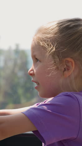 confused little girl with braid leans on chair back looking at mountains from cabin with window of ropeway close side view slow motion