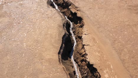 aerial view of a deep crack with water in dry terrain