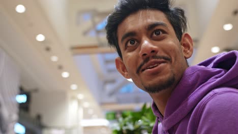 close up portrait of young indian man in an upscale shopping mall gesturing with face in slow motion