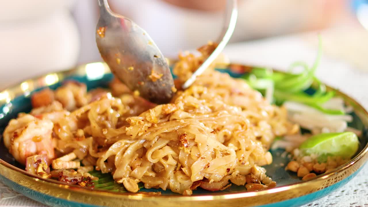 Close-up of Pad Thai being served with shrimp and lime in a vibrant Bangkok setting. Warm lighting enhances the appetizing presentation
