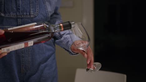 Woman-wearing-denim-clothes-pours-red-wine-into-wine-glass,-dinner-party-at-home,-evening,-alcohol-consumption,-hands,-close-up-shot,-health,-wine-tasting,-drinking,-sober,-celebration,-predrinks