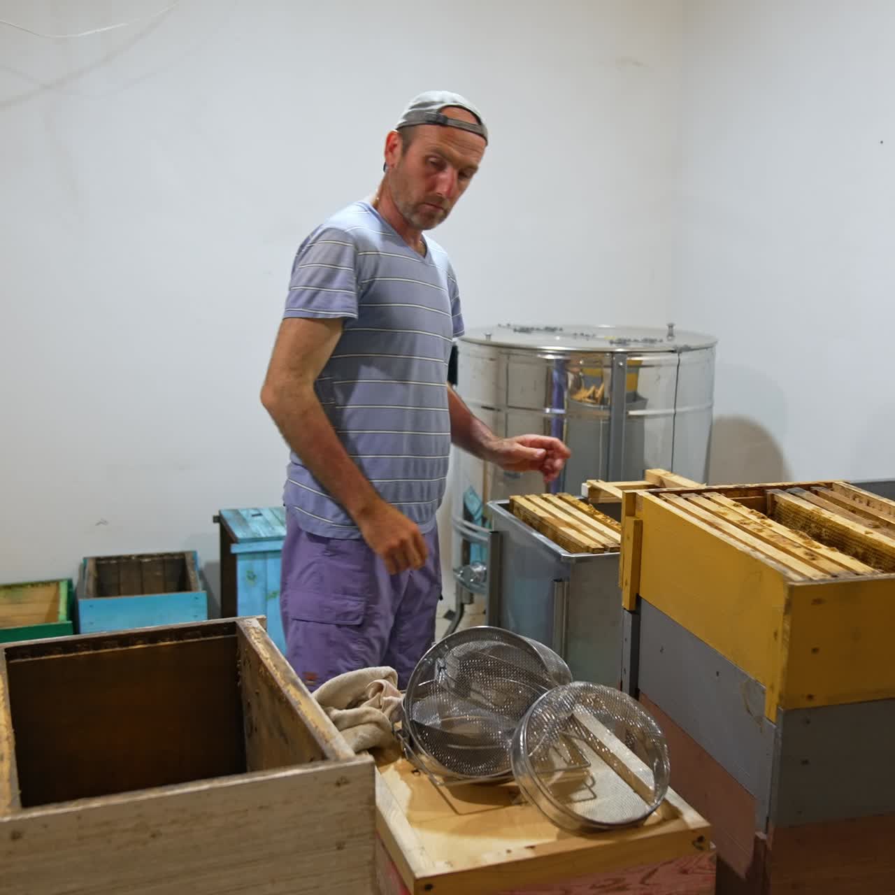 Adult beekeeper takes frames out of the wooden box and places them into the metal chest. Man stacking the empty frames after honey extraction